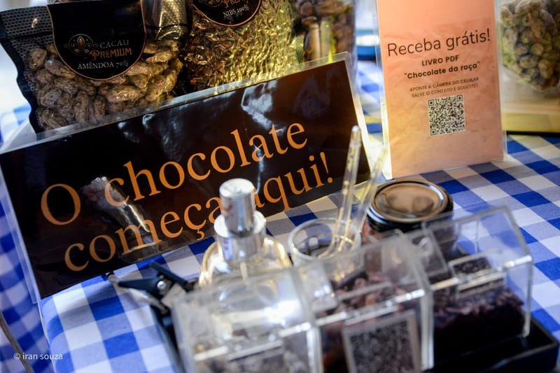 Mesa de degustação com nibs, amêndoas e a placa O chocolate começa aqui